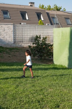 Çocuk evin yakınındaki yeşil çimlerde eğleniyor güneşli bir günde açık hava aktivitelerinin tadını çıkarıyor.