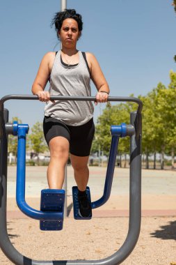 Parkta spor aletleri üzerinde egzersiz yaparak fiziksel durumunu düzelten bir kadın.