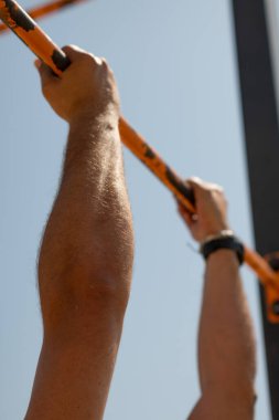 Sporcu dışarıda egzersiz yapıyor, yatay bir barda barfiks çekiyor.