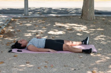 Parkta egzersiz yaptıktan sonra mindere uzanan genç kadın.