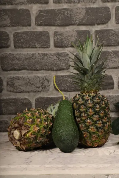 Taze Avokado ve Ananas Tuğla Duvara Karşı Mermer Masada Ayarlandı