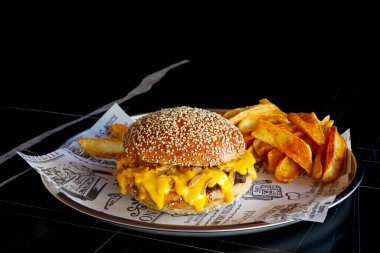 Lezzetli Cheeseburger ve yanında patates kızartması. Metal bir tabakta servis ediliyor, izole edilmiş siyah arkaplan..