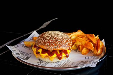 Lezzetli Cheeseburger ve yanında patates kızartması. Metal bir tabakta servis ediliyor, izole edilmiş siyah arkaplan..