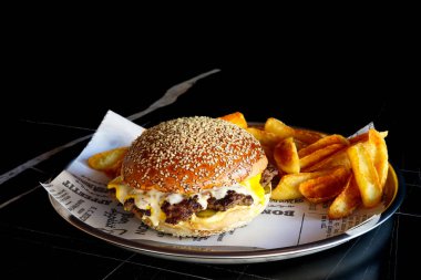 Lezzetli Cheeseburger ve yanında patates kızartması. Metal bir tabakta servis ediliyor, izole edilmiş siyah arkaplan..