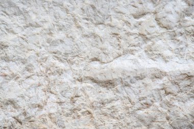 Bej ve beyaz tonlarla karakterize edilmiş doğal bir taş yüzeyin desenli yakın çekimi. Toprak dokular arka planda, tasarımlarda ve estetik projelerde kullanmak için ideal desenleri karmaşık bir şekilde sergiliyor..