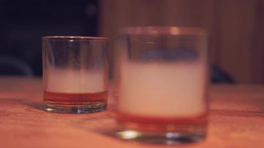 Samimi Bar Sahnesi. Yüksek kalite 4K görüntü. Kırsal bir ahşap masaya yerleştirilmiş, katmanlı bir kokteyl veya içecekle iki kısa bardağı içeren yumuşak odaklı bir görüntü..