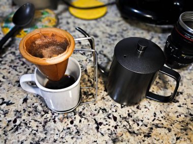 Kahve, arka planda mutfak eşyaları olan granit bir masadaki kumaş süzgecinden geçiriliyor.