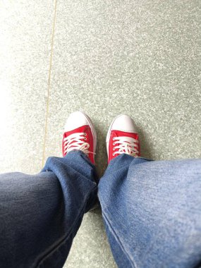 Kotlar ve kırmızı spor ayakkabılarla, gri fayansların olduğu perspektifte duruyorum.