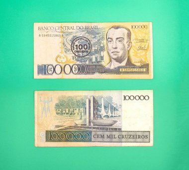 Brezilya 'dan gelen iki yüz bin cruzeiro banknotunun resmi, biri bir adamın portresi, diğeri ise modern bir binayı tasvir ediyor. Banknotlar canlı yeşil bir yüzey üzerinde sergilenerek Brezilya 'nın 39..