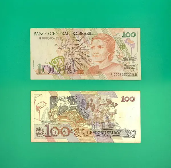 Canlı yeşil bir arkaplan üzerine iki Brezilya 100 cruzeiro notu. Üst notada tarihi bir figürün portresi yer alırken, alt notada çocuk kitapları ve doğa öğeleri yer alıyor. Brezilya ekonomisinin nostaljik bir temsili.