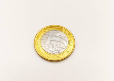 Tek hakiki bir para pürüzsüz beyaz bir yüzeye dayanır, altın ve gümüş parlaklığını vurgular. Yumuşak ışıklandırma madeni paranın ayrıntılarını vurgular, ekonomiyi ve mali değeri sembolize eder.