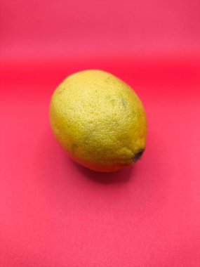 Parlak sarı bir limon canlı pembe bir zemin üzerinde uzanır, eşsiz dokusu ve çarpıcı tonu ile dikkat çeker. Görüntü tazeliği ve canlılığı çağrıştırıyor. Sağlıklı beslenme ve yaz temaları için mükemmel..