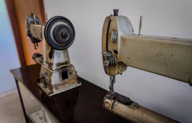 İki eski dikiş makinesi sergileniyor, eskimiş detayları vurguluyor, nötr renkler ve metalik bir doku. Sakin ortam nostaljiyi ve yıllar boyunca dikiş dikmenin evrimini anımsatıyor..