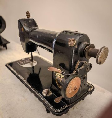 Bronz detaylara sahip klasik bir siyah metal dikiş makinesi klasik şeklini ve eski tasarımının dokusunu ön plana çıkarır. Görüntü nostaljiyi, geçmişin çekiciliğini, zanaatkarlığın ve modanın simgesini çağrıştırıyor..