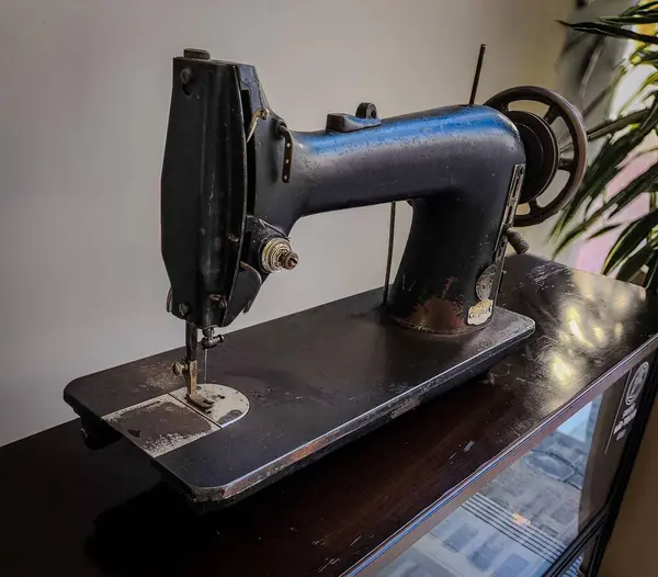 Eskimiş eski bir metal dikiş makinesi, karanlık bir yüzeye yerleştirilmiş, zamanla aşınan aşınmaların görünür detaylarını gösteriyor. Modası geçmiş tasarımı ve sağlam yapısı nostalji ve çekiciliği çağrıştırıyor. Durumunu vurgulamak için hafifçe aydınlatılıyor..