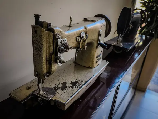 İki eski dikiş makinesi cilalı bir yüzeyde sergileniyor. İlki, eskimiş metalik kaplama ve görünür kullanım izleriyle öne çıkan ilki, geçmişe özlem uyandırıyor. Yumuşak ışık, eski makinelerin güzelliğini ve dikiş işçiliğini ön plana çıkarıyor..