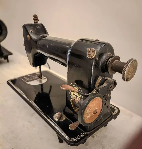 Bronz detaylara sahip klasik bir siyah metal dikiş makinesi klasik şeklini ve eski tasarımının dokusunu ön plana çıkarır. Görüntü nostaljiyi, geçmişin çekiciliğini, zanaatkarlığın ve modanın simgesini çağrıştırıyor..