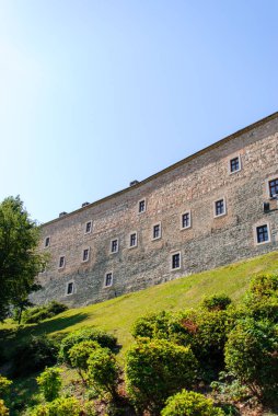 Taştan duvarları olan sembolik bir kale, canlı yeşil bir yamaca ve berrak mavi gökyüzüne karşı kurulmuş..