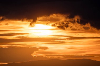Nefes kesen altın bir günbatımı gökyüzündeki dramatik, desenli bulutlara sıcak bir ışık tutuyor.