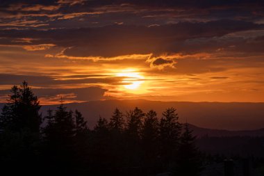 Göz kamaştırıcı bir gün batımı sahnesi zarif bir şekilde altın rengini güzel, sakin bir dağ manzarasına yansıtıyor.