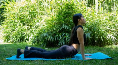 Huzurlu ve huzurlu bir an. Dışarıda yoga yapan bir kadın. Sakin ve yemyeşil bir ortamda.