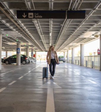 Yalnız bir gezgin boş bir otoparkta bavulu çeker. Macera, özgürlük ve keşfi simgeler.