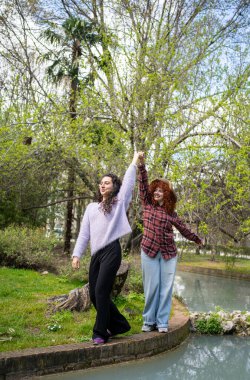 İki yakın arkadaş, yemyeşil bir parktaki güzel bir göletin kenarında neşeyle gezinip gülüyorlar.