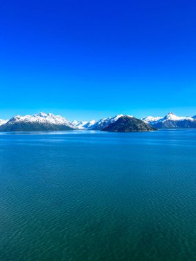 Alaska, Glacier Körfezi 'nin çarpıcı manzarası derin mavi sularını, karla kaplı dağlarını ve berrak bir gökyüzü altında huzurlu bir adayı gözler önüne seriyor. Vahşi doğa ve huzurun mükemmel bir karışımı..