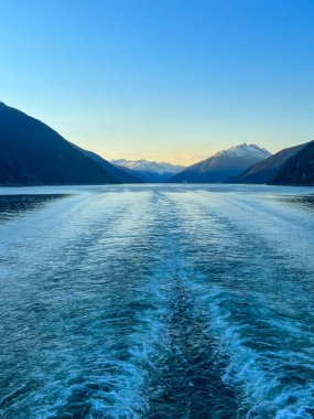 Güneş batarken Alaska fiyortlarının nefes kesici manzarası arkasında bir yolcu gemisinin huzur içinde uyanmasını sağlıyor. Karla kaplı dağlar huzurlu suları çerçeveletip doğada unutulmaz bir an yaratıyor..
