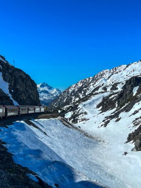 Alaska 'da karla kaplı bir dağ geçidinde nefes kesici bir tren yolculuğu. Beyaz Geçit & Yukon Demiryolu engebeli arazide esiyor, yolculara el değmemiş vahşi doğa, yüksek zirveler ve buzlu manzaralar sunuyor..