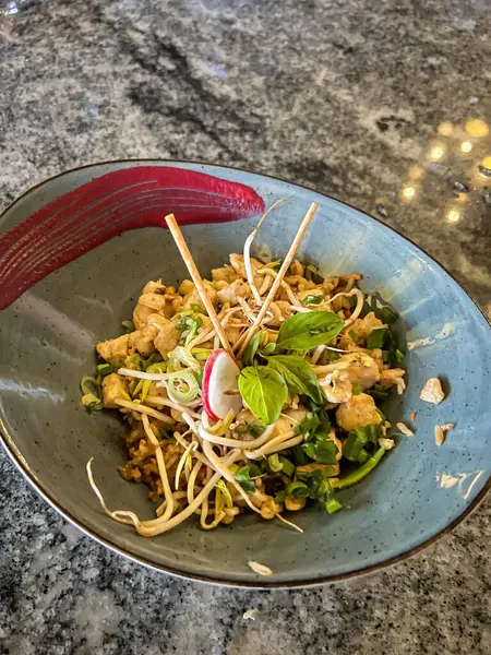 Tofu, fasulye filizleri, taze otlar ve turptan oluşan güzel bir tabakta sanatsal sos tasarımı ile servis edilen Pad Thai yemeği..