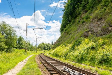 Dağ demiryolu seyahat geçmişi. Bulutlu mavi gökyüzü. Tepenin altındaki yeşil ormanın arasında demiryolu olan alp manzarası. Güneşli bir günde eski tren yolu geçidi