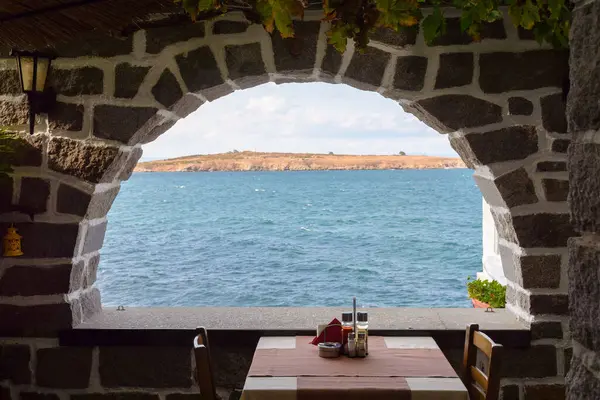 Bir kafenin penceresinden deniz manzarası. Yaz tatilleri. Güneşli bir öğleden sonra mavi gökyüzünün altında bir ada. Masalı ve iki sandalyeli ortaçağ tarzı iç mekan. seyahat otantik tatil beldesi