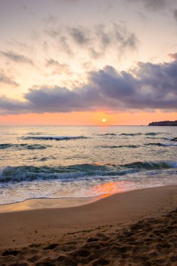 Sonbahar gündoğumunda deniz sahili manzarası. Kum kıyısında sakin bir dalga. Ufukta dramatik bulutlar var. İspanya 'da kadife sezonu tatili