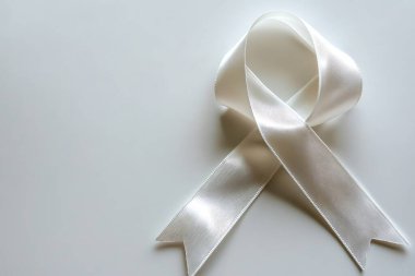 Yakından bakıldığında fildişi bir kurdelenin yumuşak dokusu ve ince parlaklığı ortaya çıkar, soluk bir arkaplan karşısında düzgünce düzenlenir, dayanışma ve destek mesajı iletir.