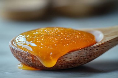 Bir makro yakın plan, koyu ahşap bir kaşıktan akan canlı turuncu marmelatları, parlak dokusunu ve keskin detaylarla yakalanan damlayan tatlılığını gösterir..