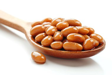 Macro çekim vitrinleri küçük kahverengi bir tahta kaşığa doldurulmuş fasulyeler, temiz beyaz bir arka fonda dinleniyor, bir fasulye yan tarafta, minimalist bir yiyecek yaratıyor..