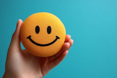 Beyaz bir el nazikçe sarı bir gülen yüz topu beşikte, siyah özellikleri parlak arka plana karşı keskin zıt, neşeli ve iyimser bir görsel oluşturur.