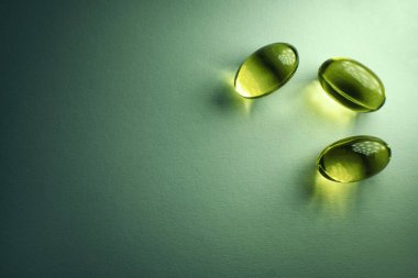 Üç ibuprofen kapsülü yeşil bir zemine gölge düşürüyor, tıp, ilaç, sağlık ve sağlıkla ilgili bir konsept görüntüsü yaratıyor, metin için geniş bir kopya alanı var.