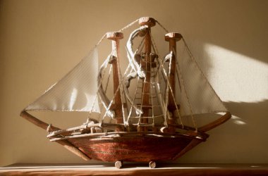 Sıcak gün ışığında yıkanan, büyüleyici ahşap model bir gemi masanın üzerinde duruyor, yelkenleri nazikçe dalgalanıyor, macera ve deniz tarihini çağrıştırıyor.
