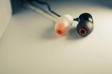 Turuncu iç bileşenlerine sahip iki kulaklık siyah bir kabloyla birbirine bağlı beyaz bir yüzey üzerinde duruyor. Minimalist ama teknolojik olarak düşündürücü bir kompozisyon oluşturuyor.