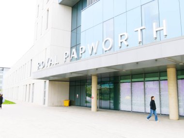 Cambridge, Cambridgeshire / Birleşik Krallık - 25 Nisan 2025: Royal Papworth Hastanesi, Cambridge, Birleşik Krallık. Gün ortası gri gökyüzü ve insanlar girişte yürüyorlar.