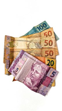 100, 50, 20, 10 ve 5 reais gibi çeşitli banknotlar, beyaz bir arka planda sanatsal olarak düzenlenmiş, para birimi tasarımı ve canlı renkler göstermektedir..