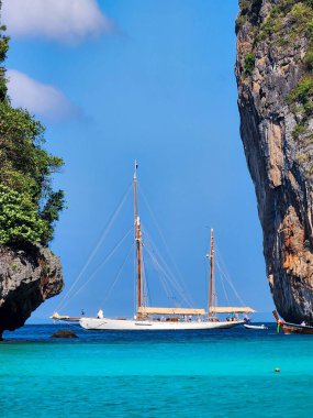 Tayland 'ın Maya Körfezi' nde kristal berrak turkuaz denizdeki kayaların arasında beyaz tekne ve uzun kuyruk teknesi.. 