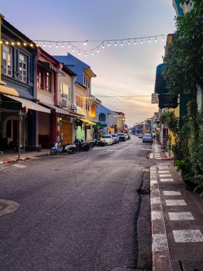Güneş doğarken renkli tarihi binaların olduğu bir şehir caddesi. Motosikletler ve arabalar park edilmiş ve sokak lambaları hala yanıyor..