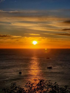 Güneş Promthep Burnu 'ndan (Phuket, Tayland) batıyor. Durgun denizin üzerindeki gökyüzünü botlarla turuncuya boyuyor. 