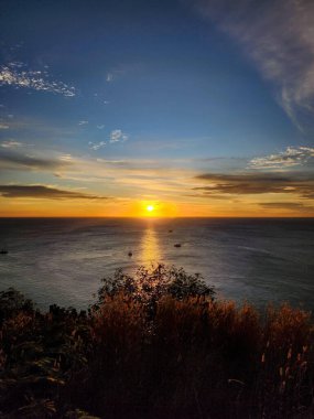 Güneş Promthep Burnu 'ndan (Phuket, Tayland) batıyor. Durgun denizin üzerindeki gökyüzünü botlarla turuncuya boyuyor. 