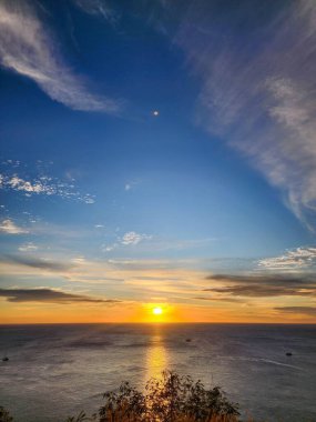 Güneş Promthep Burnu 'ndan (Phuket, Tayland) batıyor. Durgun denizin üzerindeki gökyüzünü botlarla turuncuya boyuyor. 