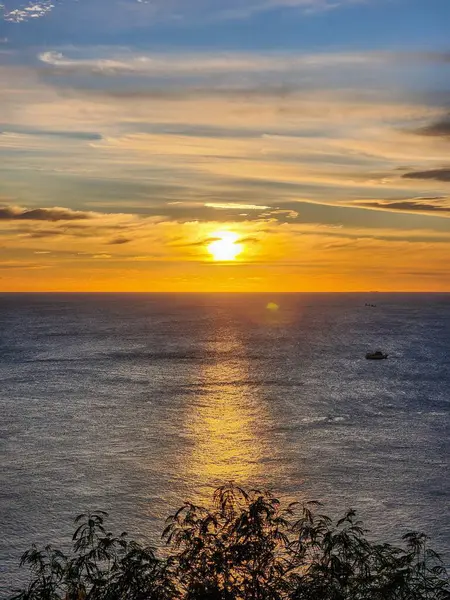 Güneş Promthep Burnu 'ndan (Phuket, Tayland) batıyor. Durgun denizin üzerindeki gökyüzünü botlarla turuncuya boyuyor. 
