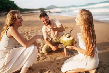 Bir grup arkadaş kumsalda huzurlu bir günün tadını çıkarıyorlar hindistan ceviziyle ve mutlu anları kucaklayarak. Yüksek kalite fotoğraf